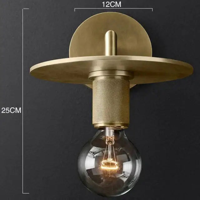 Modern brass and glass wall sconce with brass finish, circular backplate, textured stem, and exposed filament bulb