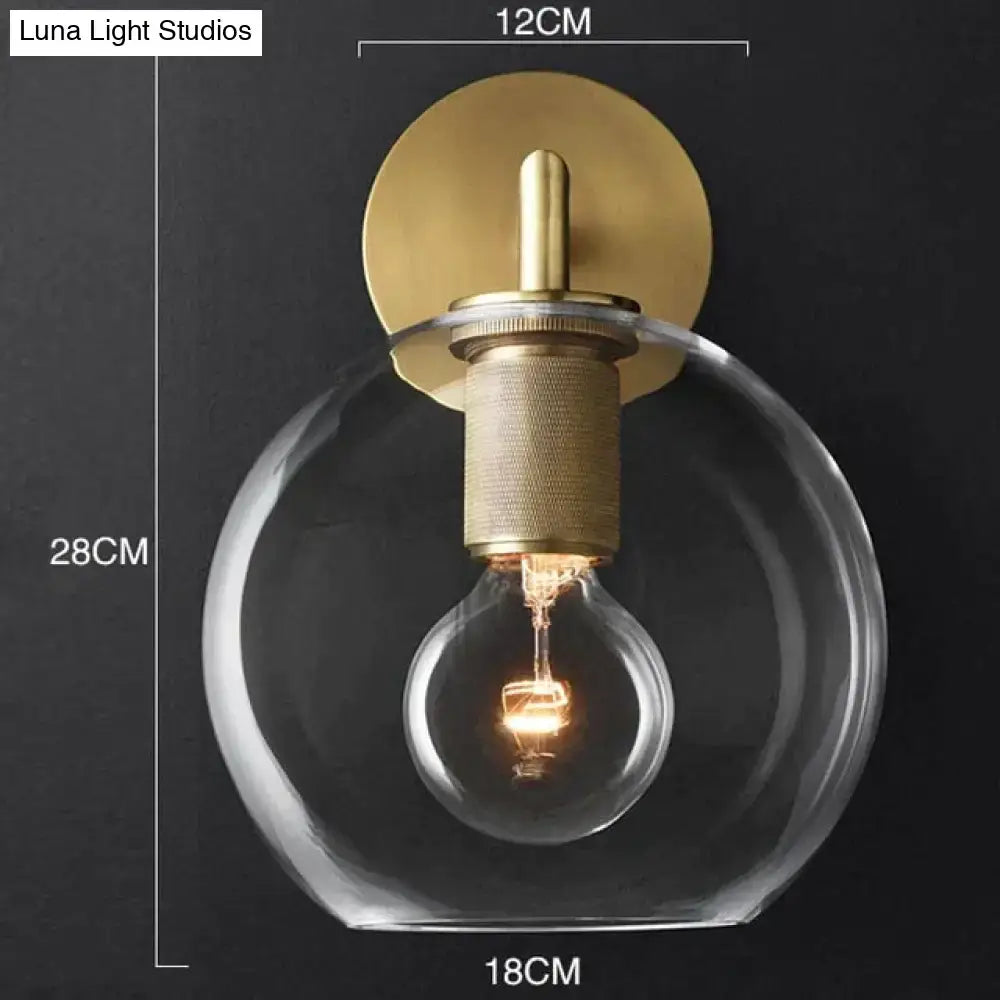 A modern brass and glass wall sconce with a clear globe and exposed filament bulb for bedroom lighting