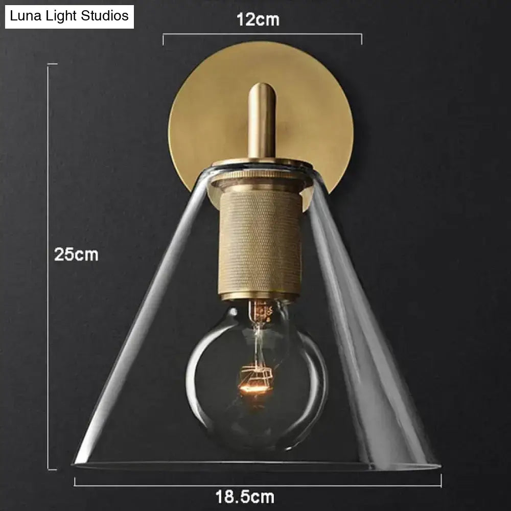 Modern brass and glass wall sconce with a clear glass conical shade and exposed filament bulb for bedroom lighting
