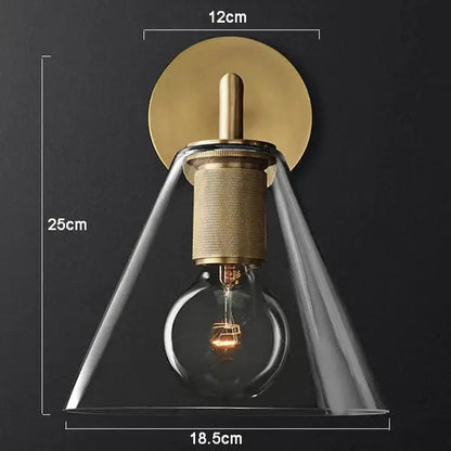 Modern brass and glass wall sconce with clear glass conical shade and exposed filament bulb for bedroom lighting