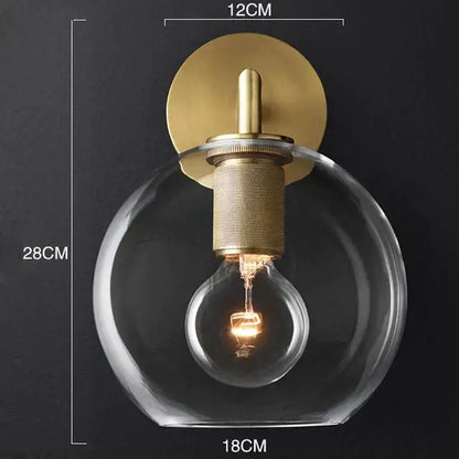Modern brass and glass wall sconce with clear glass globe and exposed filament bulb for bedroom lighting