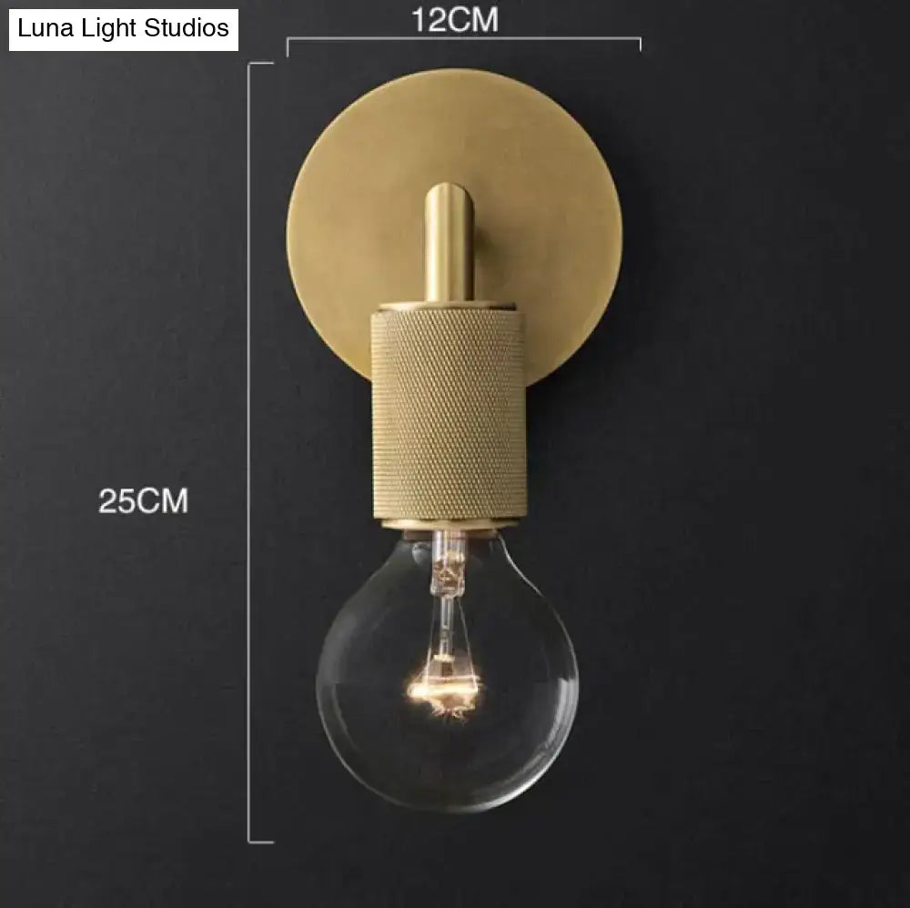 Modern brass and glass wall sconce featuring a textured cylindrical middle section and exposed bulb for bedroom lighting