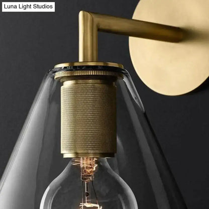 Modern brass and glass wall sconce with textured cylindrical base and clear glass shade for bedroom lighting