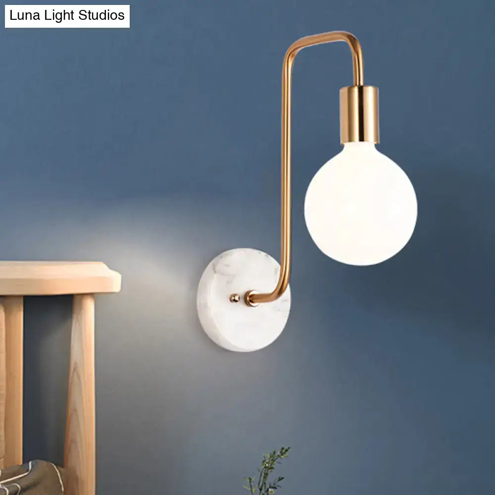 Modern wall lamp with curved brass arm white glass globe and white marble backplate for bedroom lighting