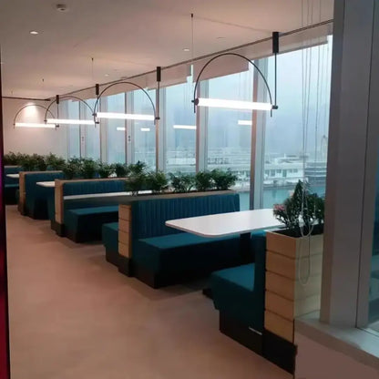 Teal upholstered booth seating with wooden panels and white tabletops under polished chrome pendant light bars