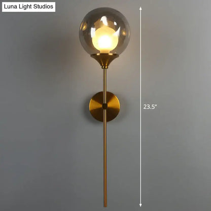 Modern brass wall light with smoke gray glass globe and slender stem ideal for bedroom sconce lighting