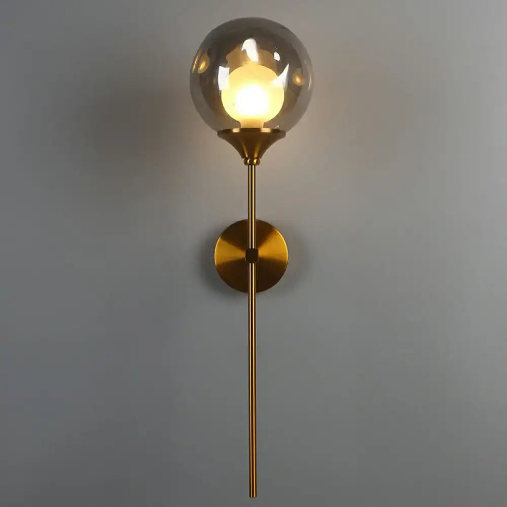 Modern brass wall light with a spherical smoke gray glass shade and slender stem for bedroom use
