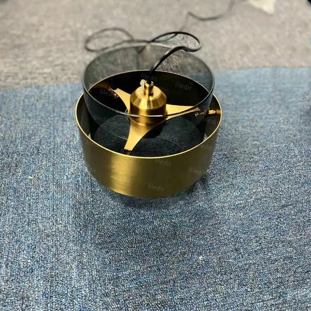 Gold-colored blender base with central motor housing and three blades inside glass container for decorbites gold wrought pendant light