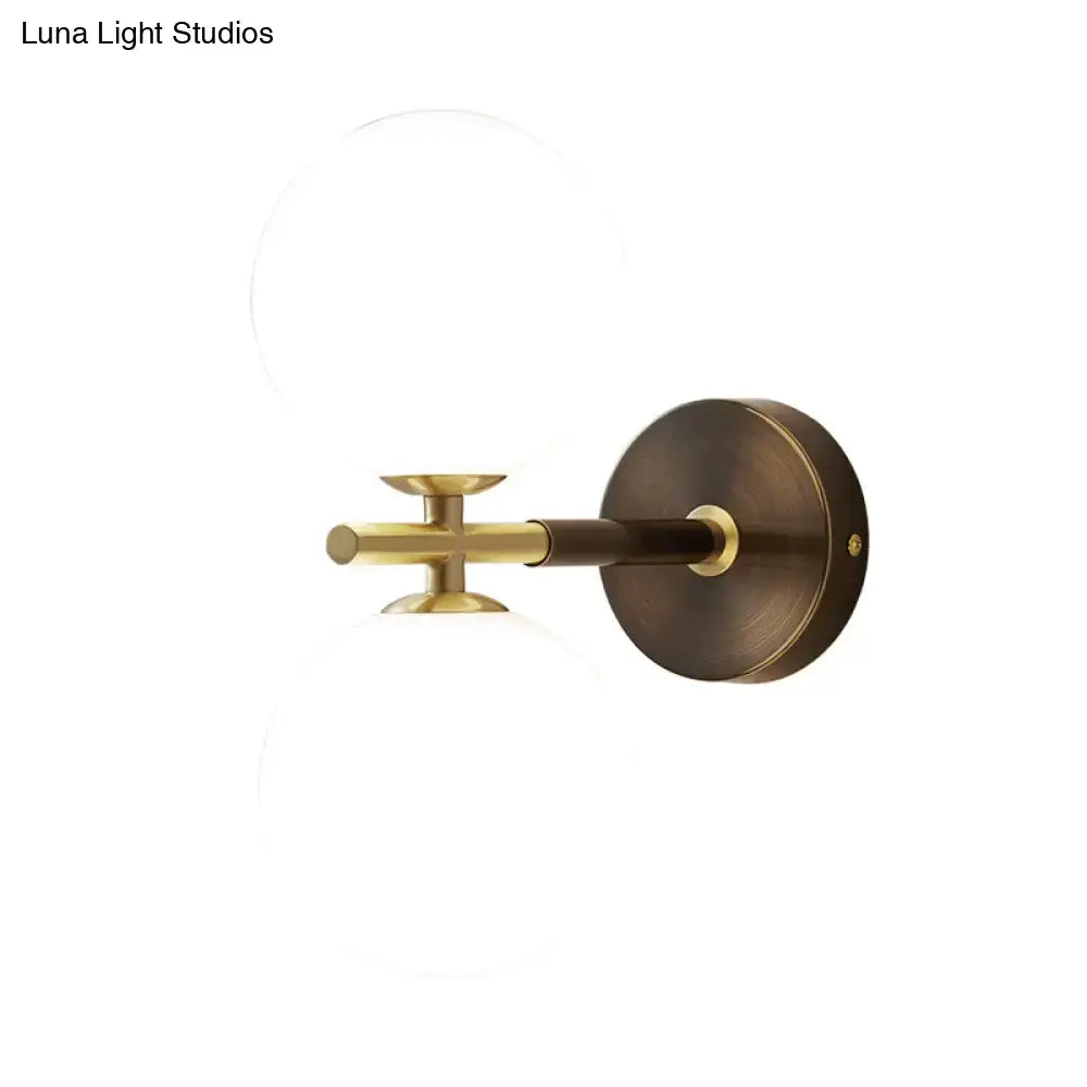 Modern brass wall sconce with white glass frosted globes and circular base for bedroom lighting