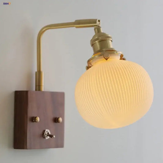 Modern brass and wood wall light fixture with ribbed frosted glass globe and dark wood mounting plate for bedroom use
