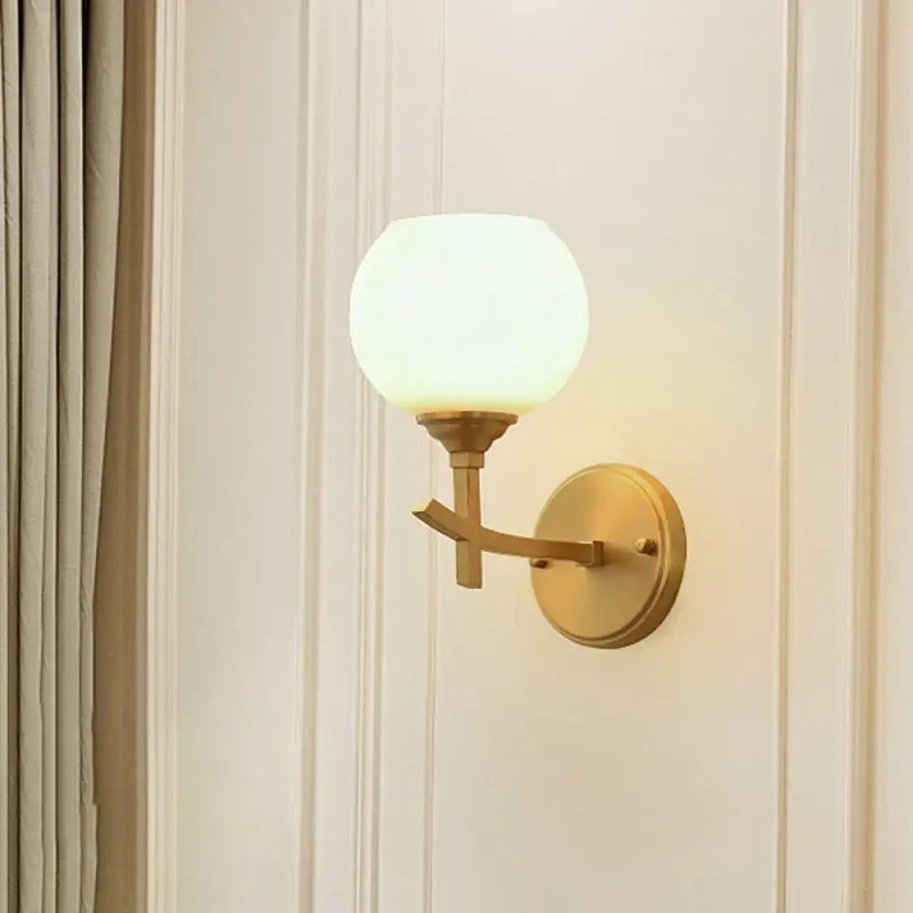 Modern brass armed wall sconce with gold tone finish and frosted opal glass shade for bedroom lighting