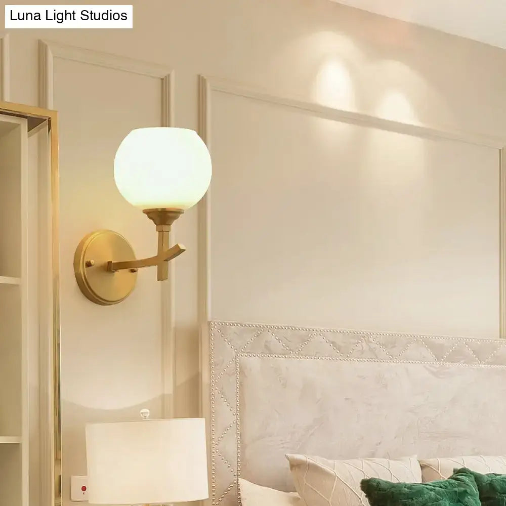 Modern brass armed wall sconce with gold tone finish and opal glass shade for bedroom lighting