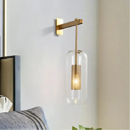 Modern brass and black wall sconce lights with clear glass housing and textured gold-finished cylindrical bulb for bedroom use