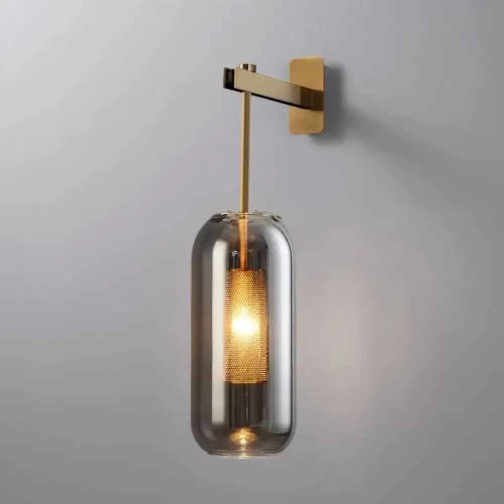 Modern brass and black wall sconce lights with a sleek brass arm and cylindrical smoked glass shade for bedroom use