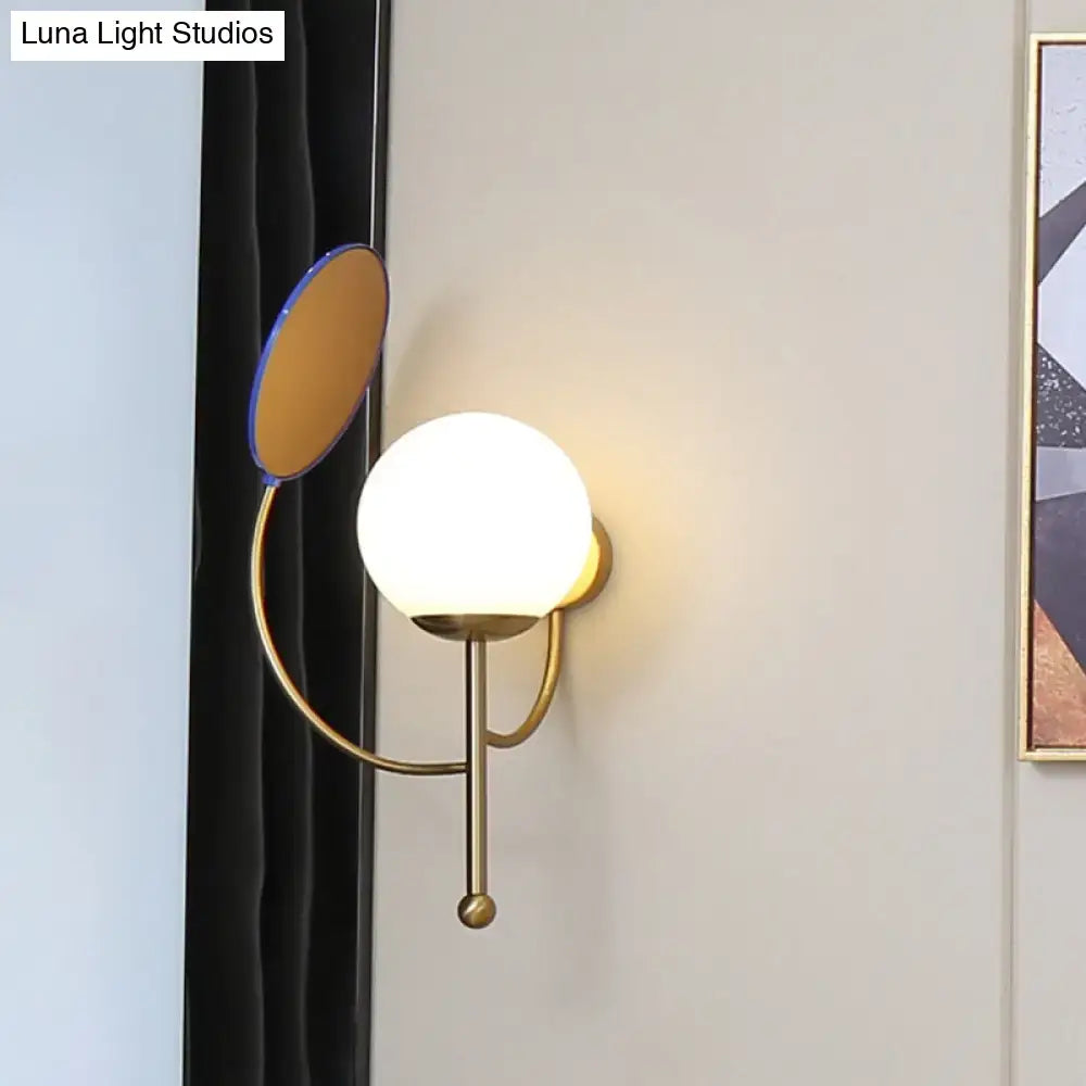 Modern brass wall sconce with white frosted glass globe and oval mirror accent for bedroom lighting