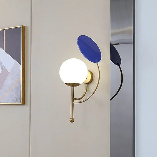Modern brass and blue wall sconce with white frosted glass spherical bulb for bedroom lighting
