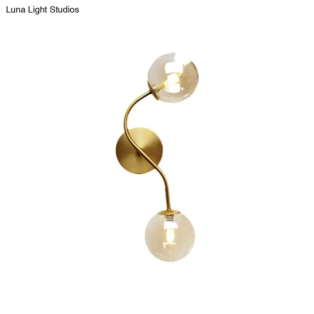 Modern brass clear tan glass wall lamp with gold-toned wall sconce and two curved arms each ending in bulb base