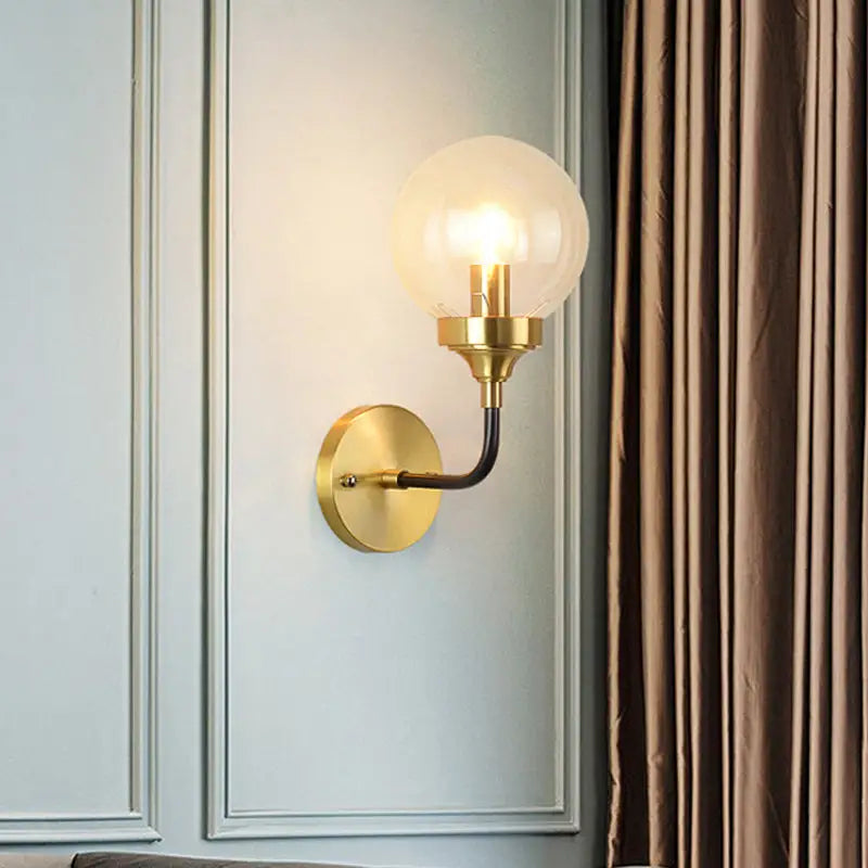 Modern brass wall sconce with a curved arm and clear glass spherical bulb for bedroom lighting