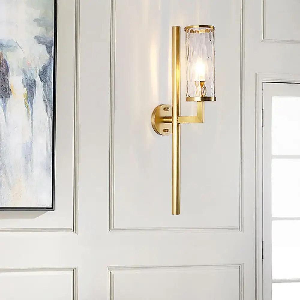 Modern brass cylinder sconce with clear water glass textured cylinder and sleek gold-toned metal arm bedroom lamp