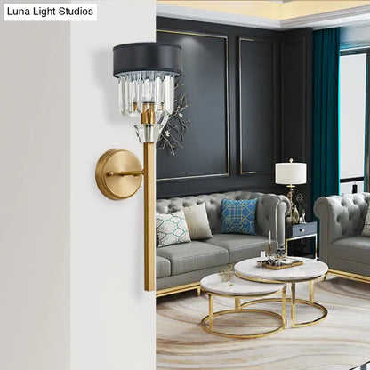 Elegant black and gold wall sconce with crystal droplets featuring a brass cylinder and fabric shade for bedroom lighting