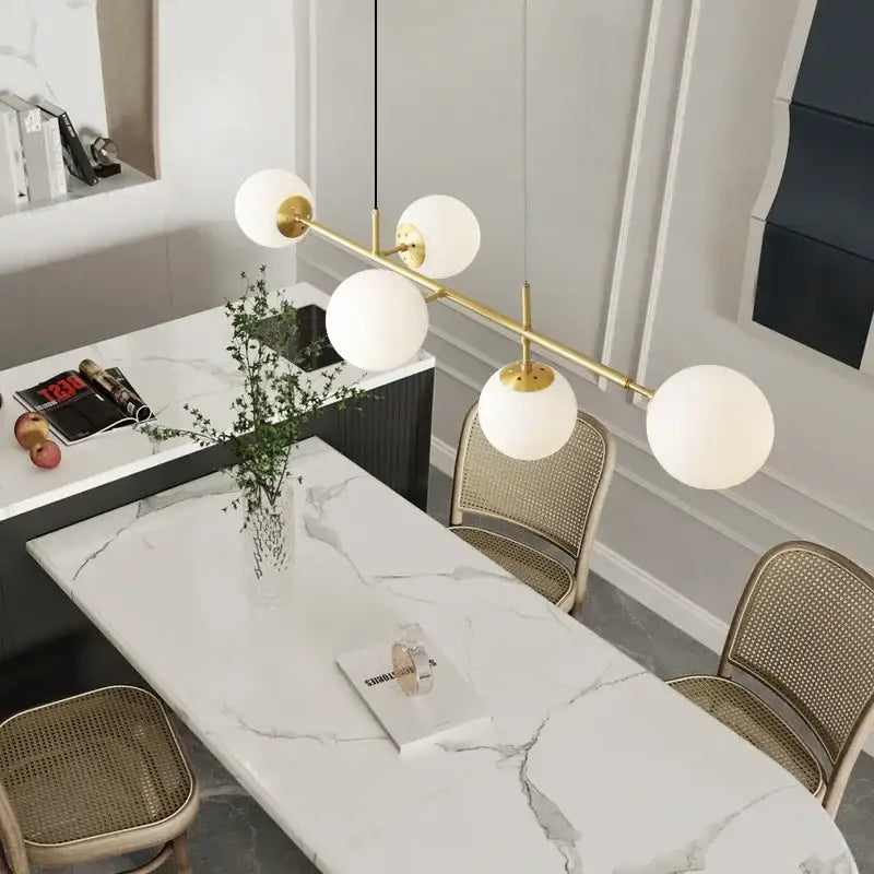 Modern brass pendant light with five golden glass ball shades featuring white spherical glass for dining room use