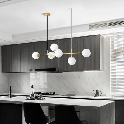 Modern pendant light with a golden glass ball design featuring five white spherical shades and a brass frame