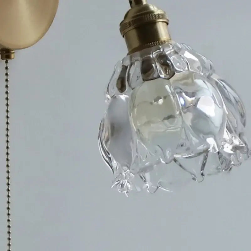 Modern brass floral clear glass wall sconce featuring a clear faceted glass lampshade with brass-finished metal fixture