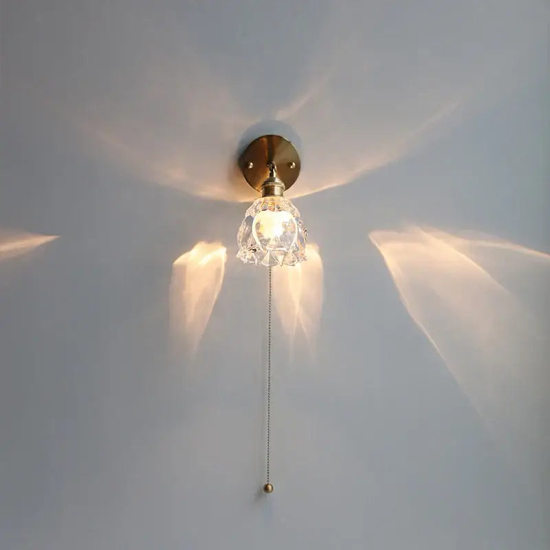 Modern brass flower glass base led wall sconce with brass finish and faceted clear glass shade casting warm light