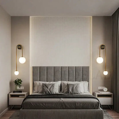 Gray tufted fabric headboard with vertical stitching paired with modern brass decorbites glass ball led wall light for bedroom