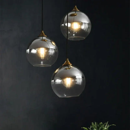 Three modern brass glass ball pendant lights with brass accents hang against a dark background for dining decorbites pendant light