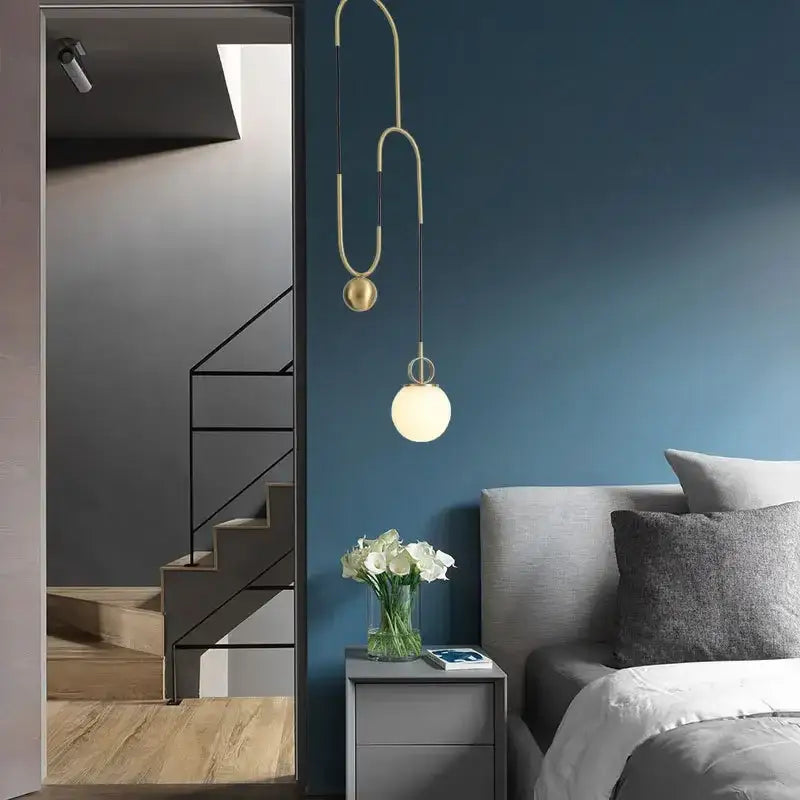 Modern brass pendant light with curved sculptural design and two glass ball pulley shades for living room decorbites
