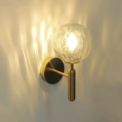 Modern brass glass ball wall lamp with a brass finish and textured clear glass globe for elegant bedroom decorbites wall lamp