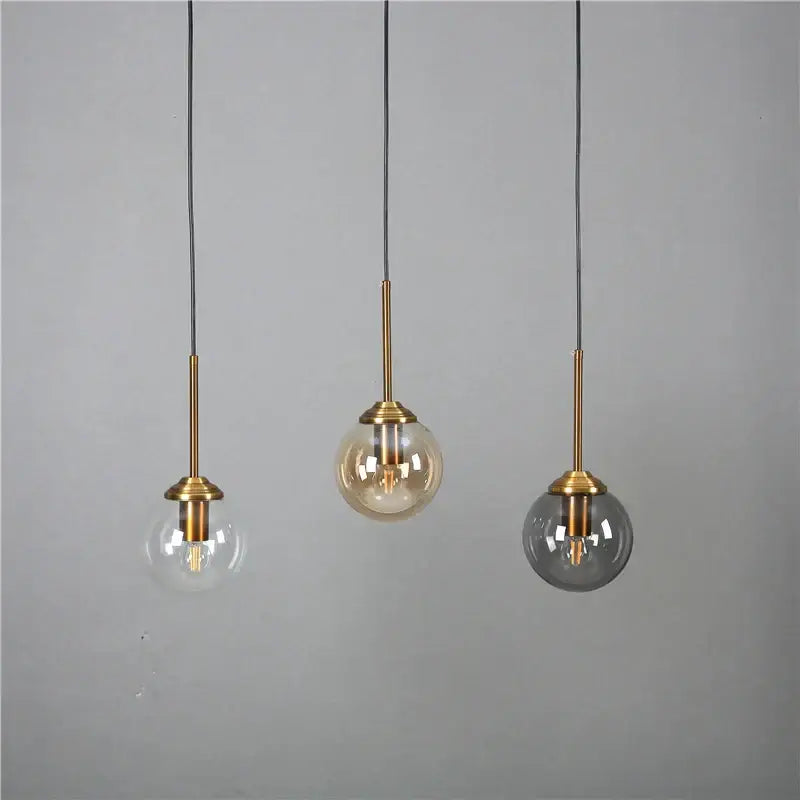 Modern brass glass ball wall lamps featuring three pendant lights with brass stems and clear, amber, and smoked glass shades