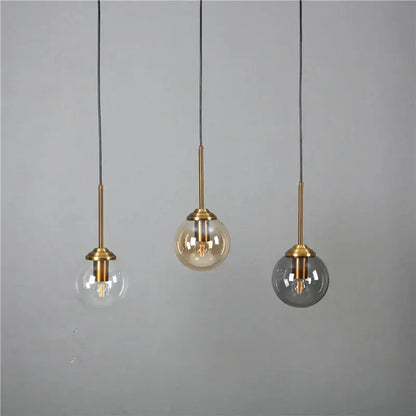 Modern brass glass ball wall lamps featuring three pendant lights with brass stems and clear, amber, and smoked glass shades