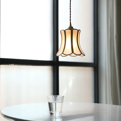 A warm-toned modern brass glass copper led pendant light with bell shape hanging from twisted cord for dining room