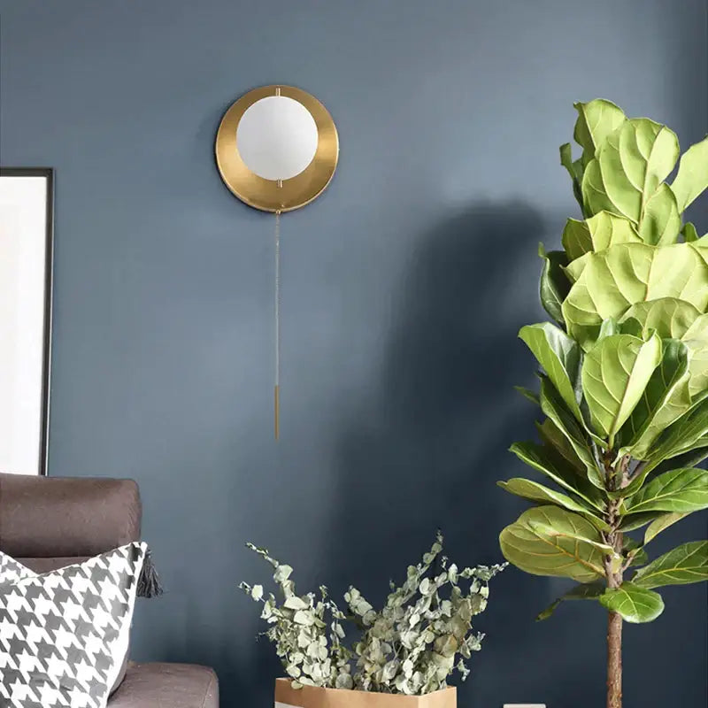 Modern brass glass round wall lamp with gold-toned circular clock face and hanging chain for bedroom lighting