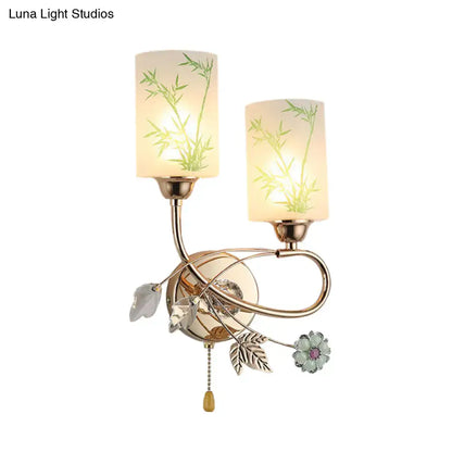 Modern brass wall lamp with pull chain featuring two frosted glass shades with green bamboo etchings