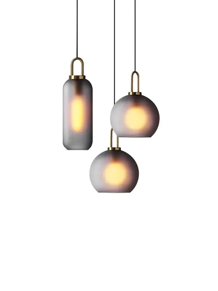 Modern brass glass staircase chandelier with three frosted gray glass pendant lights emitting warm glow