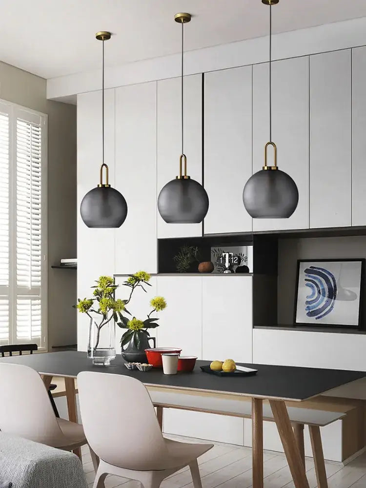 Modern brass glass staircase chandelier featuring three matte black spherical pendant lights with brass accents above dining table