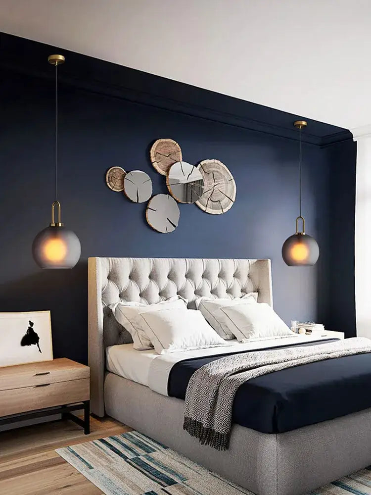 Modern brass glass staircase chandelier shown above tufted gray upholstered bed with white pillows and navy bedding