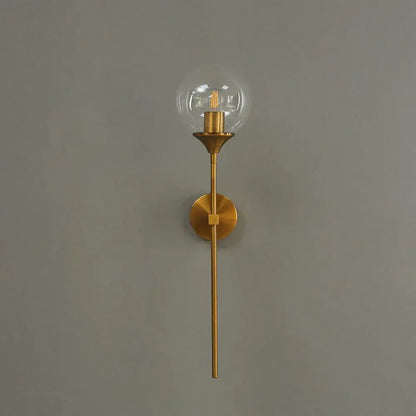 A sleek modern brass golden glass ball wall lamp with a slender stem and exposed filament bulb for bedroom decorbites