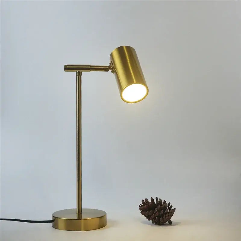 A sleek brass-finished adjustable golden table lamp with cylindrical head emitting warm light for study and reading