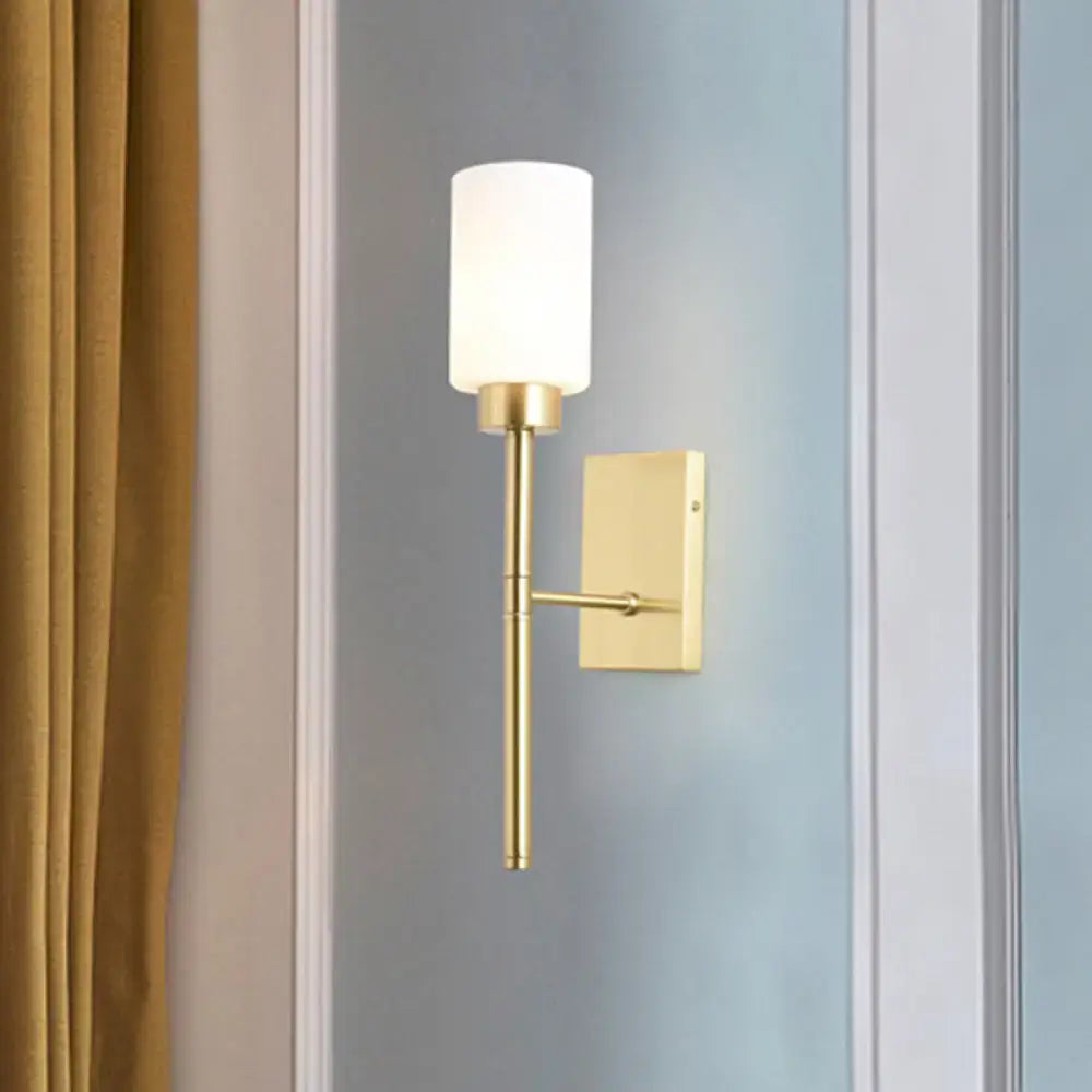 Modern brass wall light with a gold-toned frame and cylindrical opal glass tube shade for bedroom use