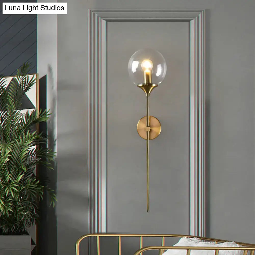 Modern brass pencil arm wall light featuring a sleek brass finish, clear glass globe, and exposed filament bulb