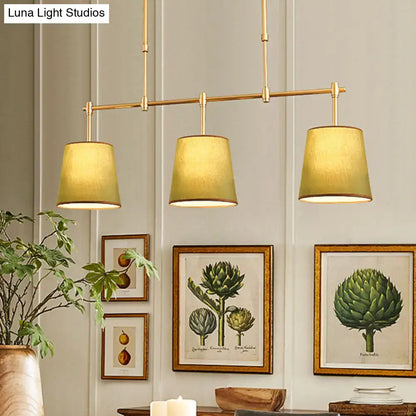 Modern brass pendant light with white green flaxen fabric shades featuring three warm-toned cylinders for dining room use