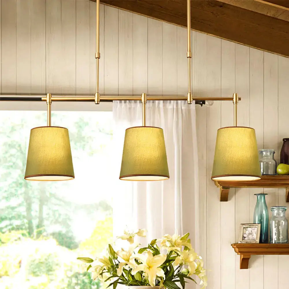 Three brass pendant lights with white green flaxen fabric shades hang in a row for dining room lighting