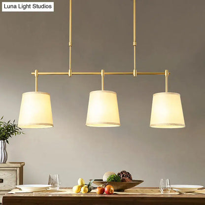 Modern brass pendant light with three cylindrical white green flaxen fabric shades for dining room lighting