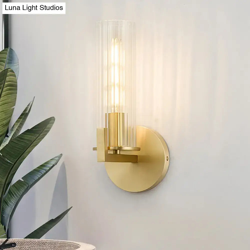 Modern brass wall sconce with gold tone finish and clear glass shade housing an exposed filament bulb for bedroom lighting