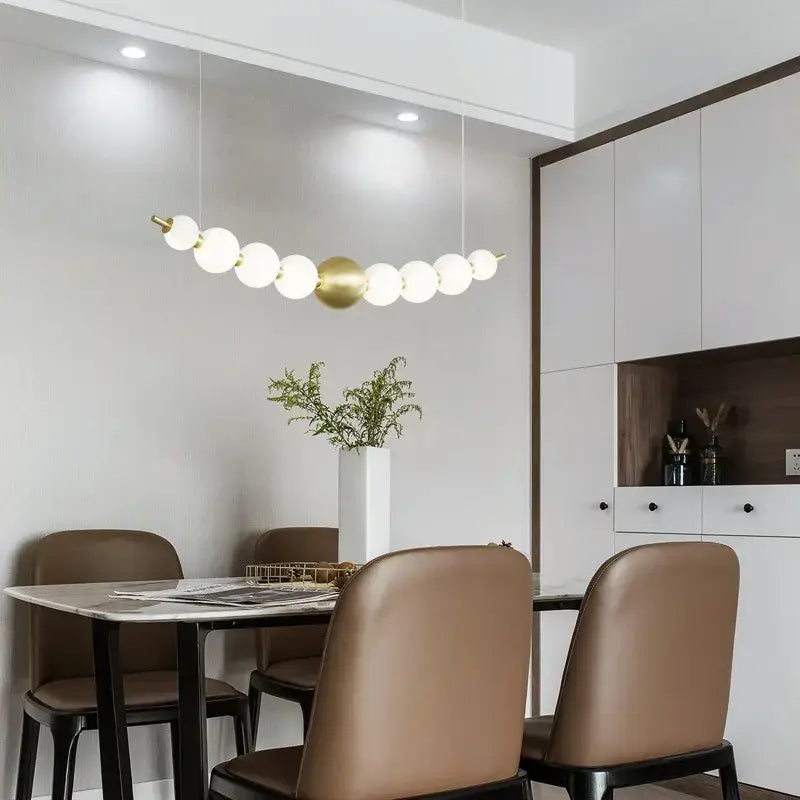 A modern decorbites brass round led pendant light fixture with white frosted glass spheres above dining table
