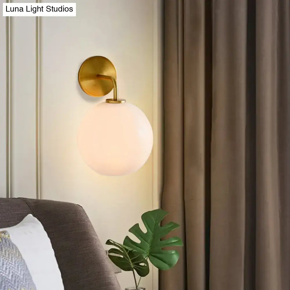 Modern brass wall lamp with gold-toned sconce and clear white frosted glass globe for bedroom lighting